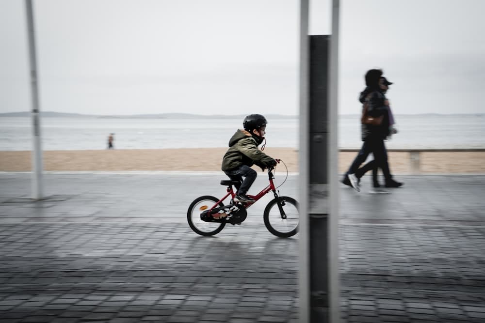Child riding a red kids bicycle along the seaside