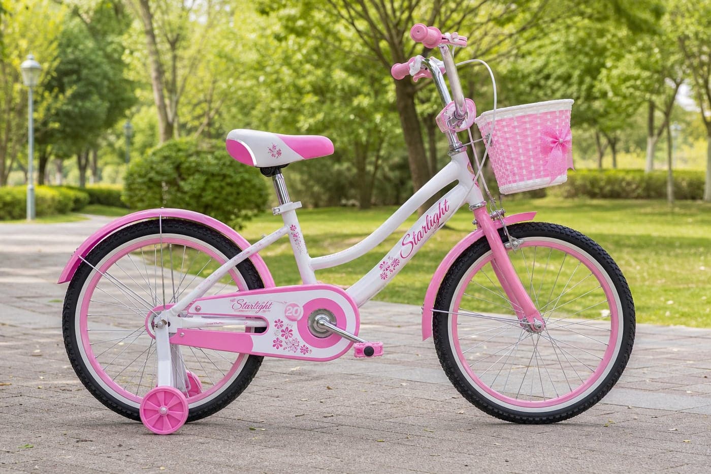 20 inch pink kids cycle with training wheels standing on a park path